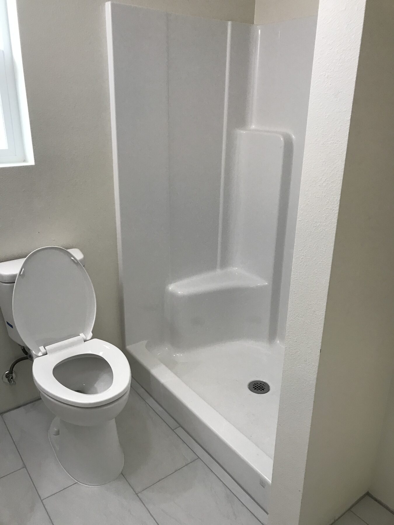 Simple white bathroom with a fiberglass shower stall, toilet and white tile floor